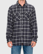 Person wearing a black and white plaid shirt with rolled-up sleeves on a gray background