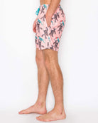 Person wearing pink swim shorts with a palm tree pattern on a white background